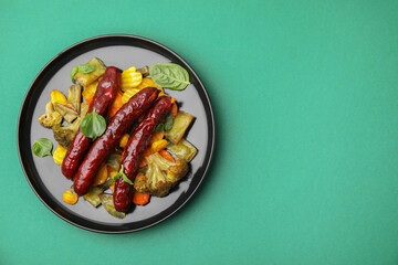 Delicious smoked sausage and baked vegetables on green background, top view. Space for text