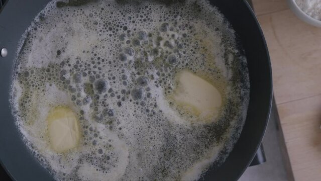 Top view of butter melting in a pan on stove in a kitchen. Butter Melting In Frying Pan Overhead Shot. Golden sizzling in frying pan on stove. Close-up shot. 