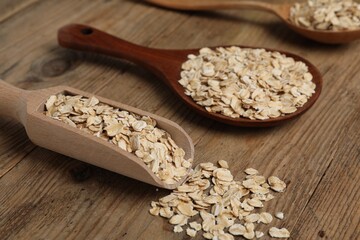 Scoop and spoons with oatmeal on wooden table, closeup
