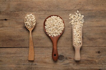 Scoop and spoons with oatmeal on wooden table, flat lay