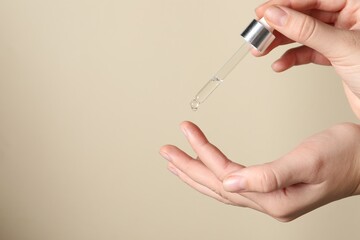 Woman applying cosmetic serum onto finger on beige background, closeup. Space for text