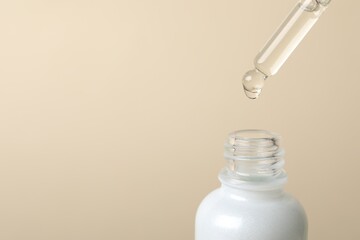 Dripping cosmetic serum from pipette into bottle on beige background, space for text