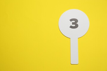 Auction paddle with number 3 on yellow background, top view. Space for text