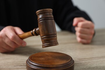 Judge with gavel sitting at wooden table against light grey background, closeup