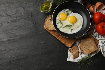 Frying pan with tasty cooked eggs and other products on black table, flat lay. Space for text