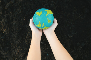 Young boy's hand holding planet Earth globe on fertile soil background as Earth day to save this...