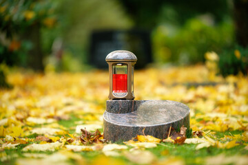 grave lantern on an urn gravestone in a meadow covered with autumn leaves