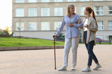 Senior lady with walking cane and young woman outdoors. Space for text