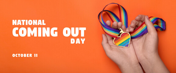 National Coming Out day, October 11. Woman holding rainbow ribbon with heart shaped pendant on orange background, top view. LGBT pride