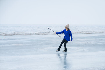 A caucasian woman is skating on a frozen lake holding a selfie stick in her hands. The figure...