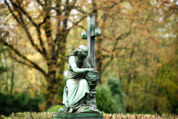 a female funerary figure sits mournfully at the foot of a cross with an urn against a blurred...