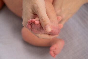 A young mother holds the foot of her newborn son with a bruise from neonotal screening. Close-up of...