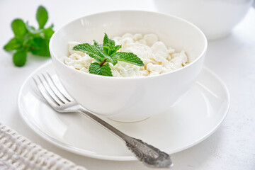 Fresh cottage cheese in granules in a white cup on a white background