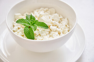 Fresh cottage cheese in granules in a white cup on a white background