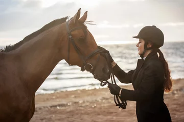 Foto op Canvas Equestrian sports. Horsewoman and her horse on the beach, portrait on the background of the sea, horseback riding outdoors © Ulia Koltyrina