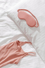 Top view pink pajama and eye sleep mask on white crumpled bedclothes, cushion and blanket. Cozy pyjamas for comfort rest at night. Flat lay from singlet, shorts, sleeping mask pastel pink color