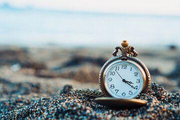 a gold pocket watch rests on sandy shores, framed by the gentle backdrop of beach waves