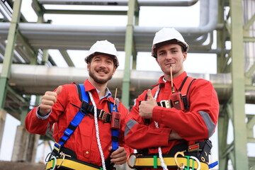 Portrait of two male engineers with full body harnesses in orange safety uniforms at the pipeline...