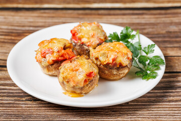 A plate with stuffed baked mushrooms with tomato and cheese on wooden background, side view, close up