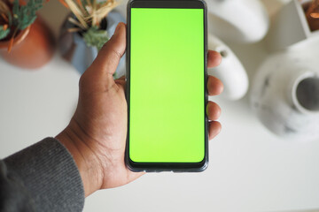 holding smart phone with green screen and home interior decoration on table 
