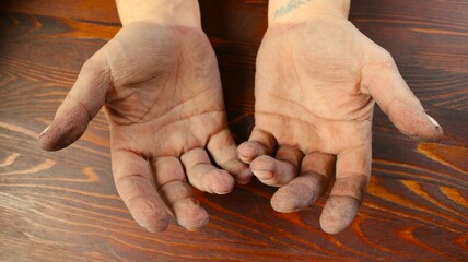 dirty male hands lying empty palms up on a brown textured wooden surface, the working hands of a...