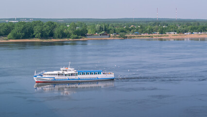 A small white motor ship is sailing on a wide river. An old pleasure boat. Recreation of people on the river. Entertainment for people associated with sailing on a motor ship. River transport.