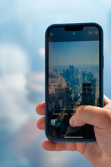 A young man takes a picture of a tall building in Dubai with his mobile phone. - obrazy, fototapety, plakaty