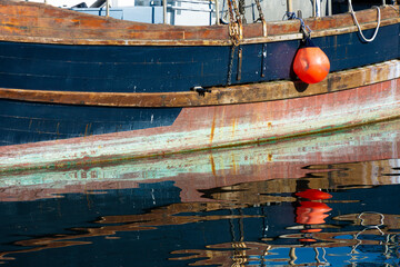 A clear water reflection of the hull on an old wooden boat with a bright red buoy. 