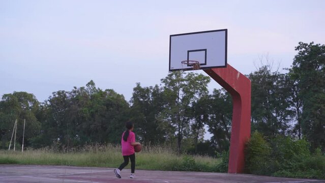 asian child or kid girl playing basketball to jumping training shooting at old basketball court and hoop broken net or rope in school park and lack poor for fun exercise with sports equipment ruined