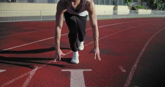 Young african american man doing star pose at starting point before running exercise on track in sport stadium