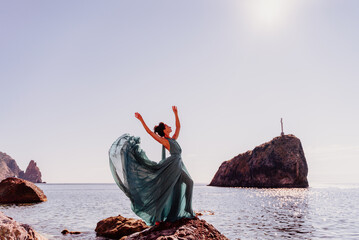 Woman green dress sea. Woman in a long mint dress posing on a beach with rocks on sunny day. Girl on the nature on blue sky background.