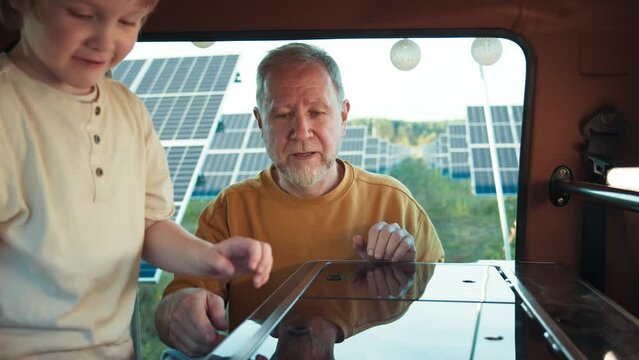 Grandfather engaging with young grandson in the kitchen of a camper van. Solar panels in the background, atmosphere tranquil moment during a vacation.