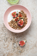 Roseate bowl with granola, greek yogurt and torn figs, above view on a beige granite background, vertical shot