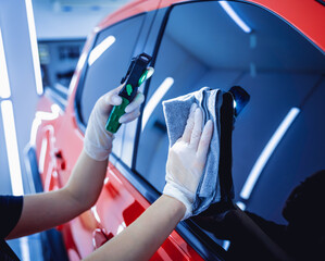 Car detailing worker cleaning and polishing car with microfiber cloth and vacuum.