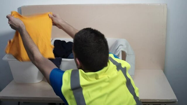 Concept, dificulties of textile recycling, color separation. Mix composition and color. Operator works at a textile sorting plant, classifying garments by colour. Holding blue, orange and white