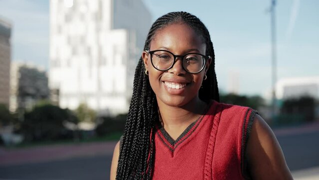African American woman with braids and eyeglasses looking at camera smile in the urban city
