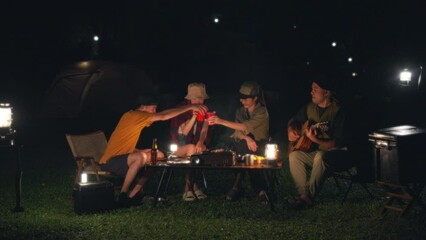 Happy asian diverse group friends enjoy drinking a beer together. They feeling relaxed and refreshing while camping in the nature at night. Recreation and journey outdoor activity lifestyle.