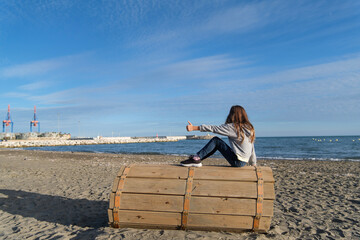 Niña en la playa, vista de espaldas, octubre, pelo largo suelto, jugando en la arena, sentada,...
