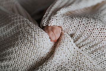 Close-up of a Caucasian baby's small hand and a knitted blanket