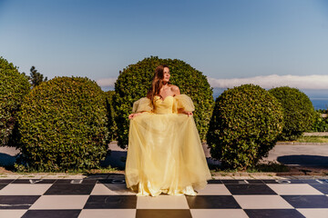 Woman yellow dress chess. A beautiful woman in a long puffy yellow dress poses on a chessboard in...