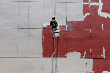 construction workers are painting the exterior of a building on dangerous scaffolding hanging from a tall building.  climbing walls to paint the walls of skyscrapers