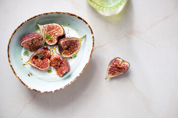 Green bowl with fresh torn figs and yogurt, flat lay on a beige granite background, horizontal shot with space