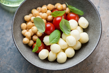 Olive-colored bowl with scamorza, smoked perlini, cherry tomatoes and fresh green basil, middle close-up, horizontal shot