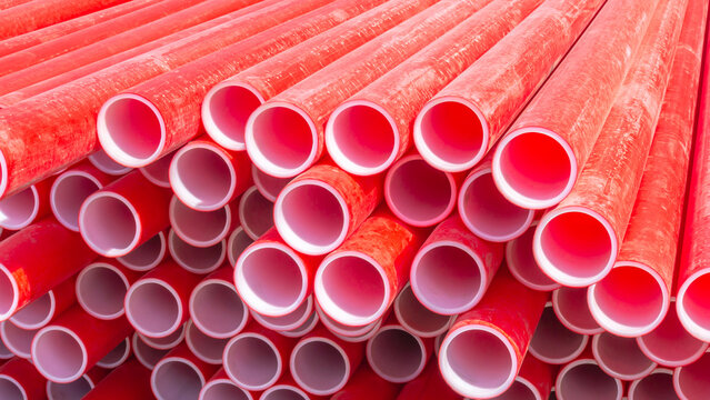 Red polyvinyl chloride pipes for laying electrical cables. Plastic pipe for carrying out communications during construction and repair. Laying pipes in trenches. Background of red long pipes.