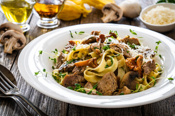 Tagliatelle with roast pork loin, parmesan cheese and mushrooms served on wooden table
