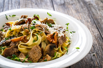 Tagliatelle with roast pork loin, parmesan cheese and mushrooms served on wooden table
