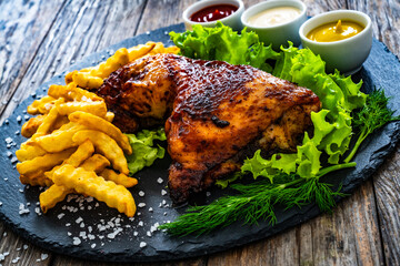 Roasted chicken thigh with French fries, lettuce and tomato on wooden table
