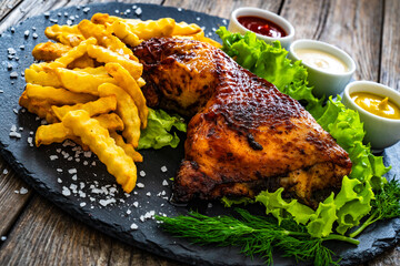 Roasted chicken thigh with French fries, lettuce and tomato on wooden table
