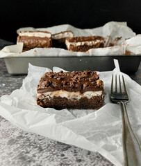 Chocolate mint brownie with fondant and ganache (side view of a square of brownie on white parchment with a fork)
