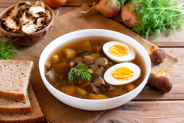 White plate with soup with mushrooms and egg. Wooden background, bread and spices
